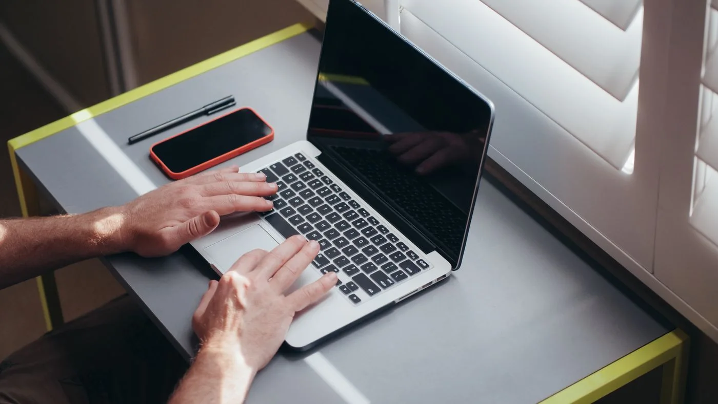 Hands typing on a laptop beside a window.